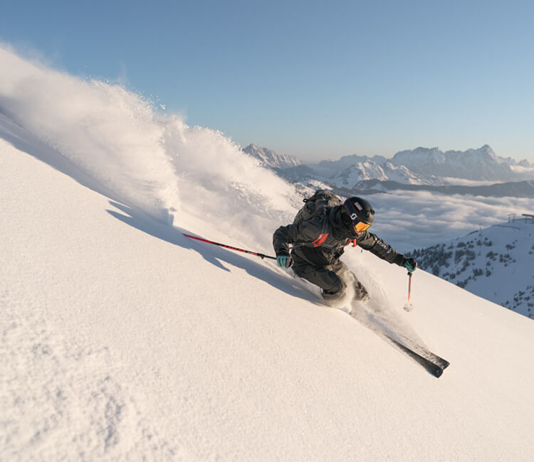 Ein Skifahrer carvt durch den frischen Pulverschnee einer steilen Piste im Salzburger Land, mit einer atemberaubenden Aussicht, die das alpine Erlebnis des Hotel Brandgut unterstreicht.